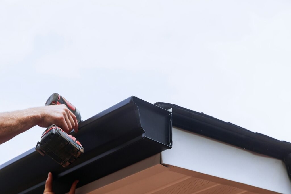 Worker installing rain gutter on roof is mounting a downpipe